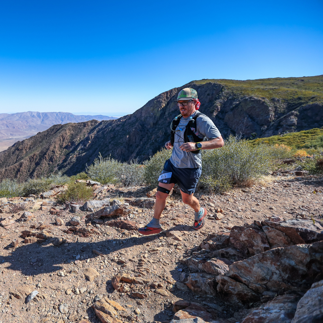 Man running on a rocky trail with mountains in the background