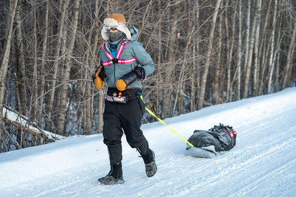 Runner participating in the Arrowhead 135 race, pulling a sled through snowy terrain.